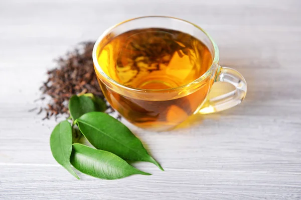 Glass cup of black tea with green leaves on grey wooden background — Stock Photo, Image