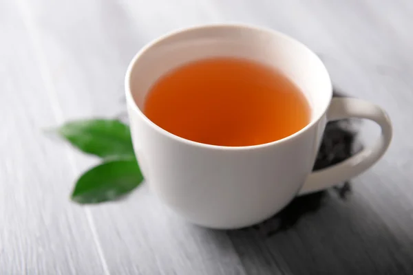 Ceramic cup of tea with scattered tea leaves around on light wooden background — Stock Photo, Image