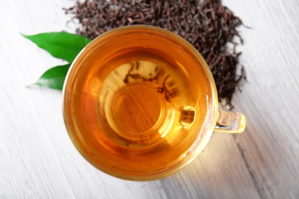 Glass cup of black tea with green leaves on grey wooden background — Stock Photo, Image