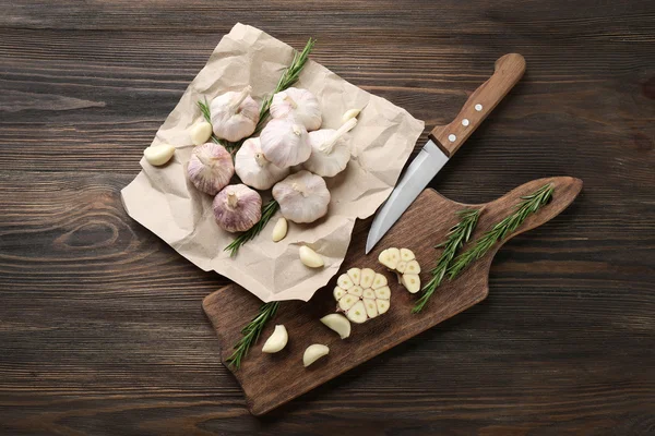 Složení česneku a rozmarýnu s nožem na kuchyňské desce, zblízka — Stock fotografie