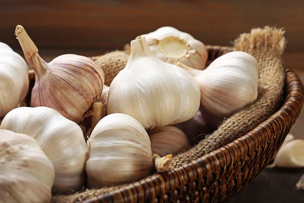 Garlic in wicker bowl on wooden background, close up — Stock Photo, Image