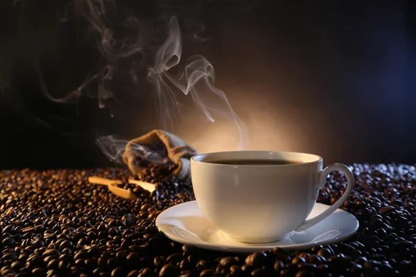 Kopp varm kaffe bland kaffebönor på mörk bakgrund — Stockfoto