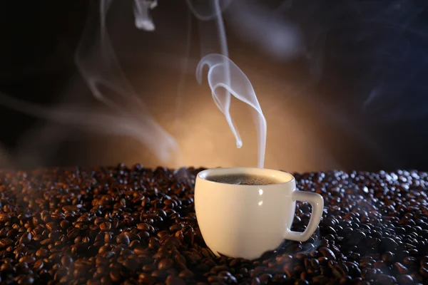 Tasse heißen Kaffee zwischen Kaffeebohnen auf dunklem Hintergrund — Stockfoto