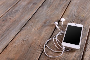 Kulaklıklarla ahşap arka plan üzerinde beyaz cep telefonu