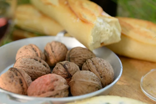 Piknik koncept - víno, lahodný sýr, vlašské ořechy a bagetou na dřevěné desce, zblízka — Stock fotografie