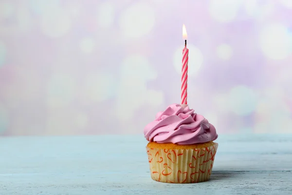 Süßer Cupcake mit Kerze auf blauem Holztisch vor verschwommenem Hintergrund — Stockfoto