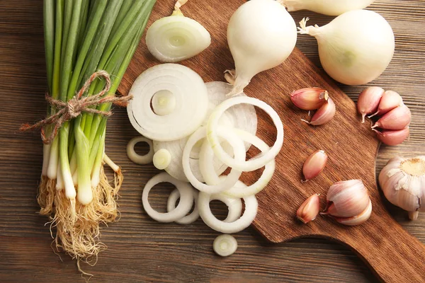 Lök cirklar, färsk grön lök med vitlök ombord mot trä bakgrund — Stockfoto