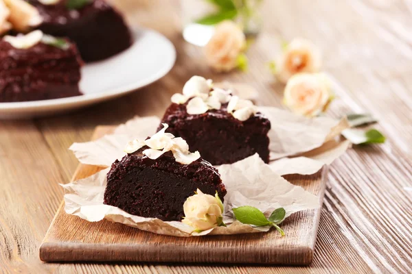 Pièce de gâteau au chocolat décorée de fleurs sur une table en bois marron — Photo