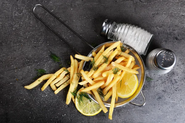 French fries with lemon and salt in sieve on table — Stock Photo, Image