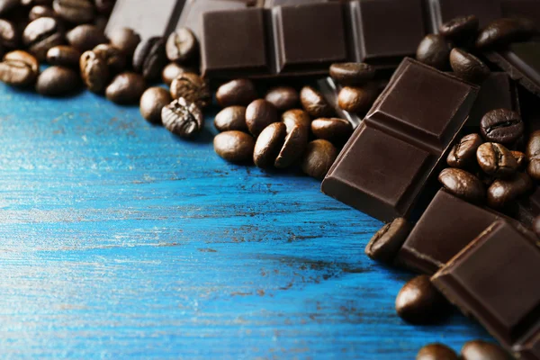 Schwarze Schokoladenstücke und Kaffeekörner auf farbigem Holzhintergrund — Stockfoto
