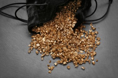 A pouch with scattered gold nugget grains, on cement background clipart