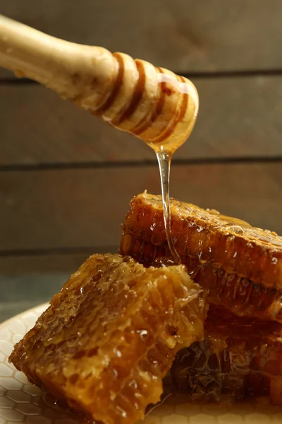 Mel pingando em favos de mel, em fundo de madeira — Fotografia de Stock