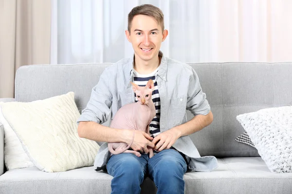 Junger schöner Mann sitzt mit Katze auf Couch zu Hause — Stockfoto