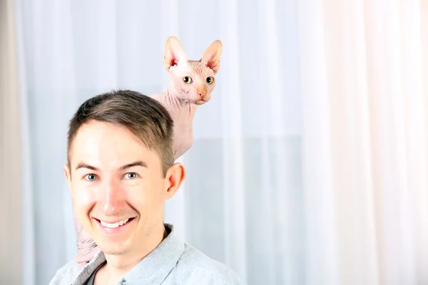 Jonge knappe man met een kat op lichte tulle achtergrond — Stockfoto