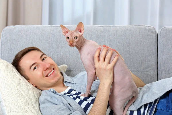 Mladý pohledný muž leží s kočkou na gauči doma — Stock fotografie