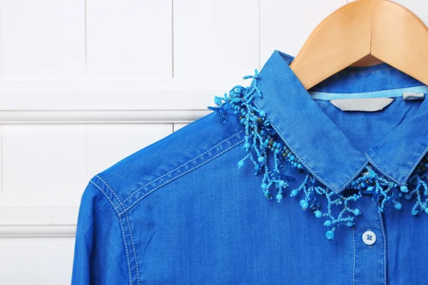 Denim shirt and necklace on hanger on wall background — Stock Photo, Image