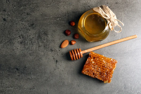 Nido de abeja, maceta de vidrio con miel y nueces sobre fondo gris —  Fotos de Stock