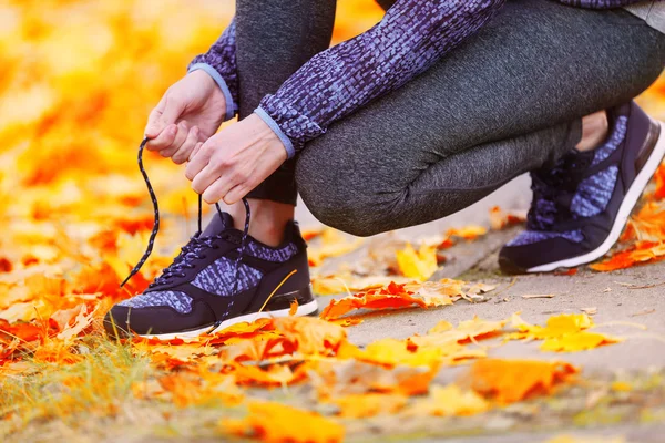 Женщина в спортивной одежде завязывает шнурки на кроссовках на открытом воздухе крупным планом — стоковое фото