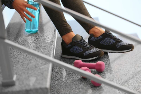 Sports woman in sneakers sitting on stairs — Stock Photo, Image