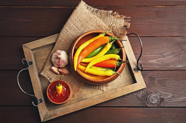 Kleurrijke chilipepertjes in kom en smakelijke saus in kom, op dienblad, close-up — Stockfoto