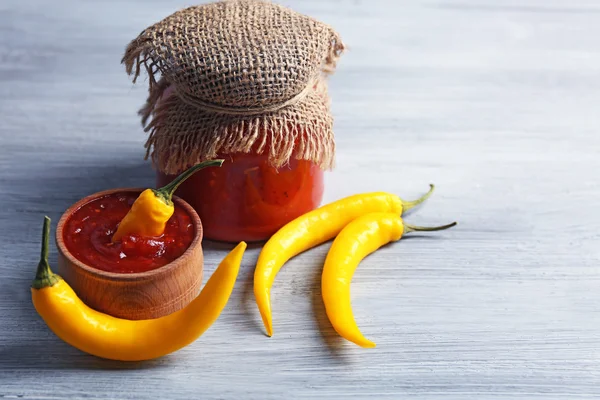 Yellow chili peppers and tomato sauce on light wooden background — Stock Photo, Image