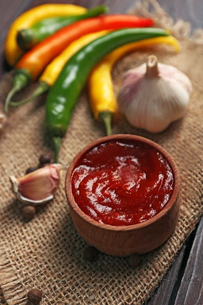 Salsa picante casera y especias sobre tela de saco, sobre fondo de madera — Foto de Stock