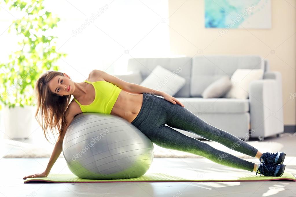 Beautiful young girl doing exercises with fit ball at home