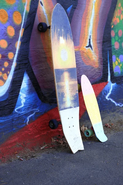 若い女性スケート ボード塗られた壁の背景にアスファルトの上に座って — ストック写真