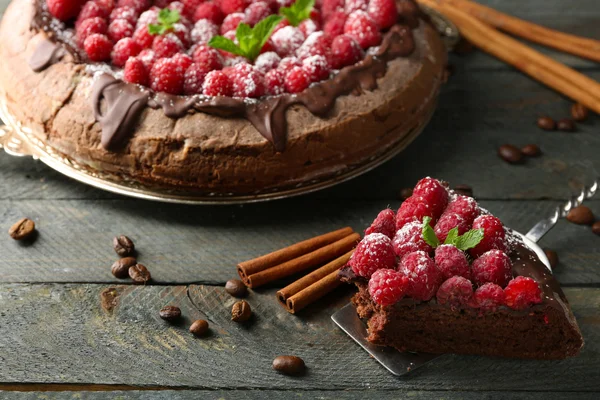 Stück Kuchen mit Schokoladenglasur und Himbeeren auf farbigem Holzhintergrund — Stockfoto