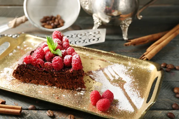 Pezzo di torta con glassa al cioccolato e lamponi su vassoio su sfondo di legno — Foto Stock
