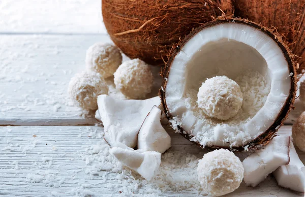 Candies in coconut flakes and fresh coconut on  light wooden background — Stock Photo, Image