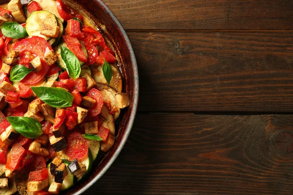 Smakelijke vegetarische ratatouille gemaakt van aubergines, squash, tomaten en uien in zwart gietijzeren pan, op houten tafel achtergrond — Stockfoto
