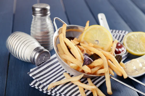 Patatas fritas en colador de metal con salsa sobre fondo de madera — Foto de Stock