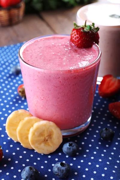 Vasos de batido frío fresco con frutas y bayas, sobre fondo de mantel azul — Foto de Stock