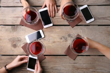 Kırmızı şarap, gözlüklü ahşap masa arka planda tutarak akıllı telefonlar ile dört el