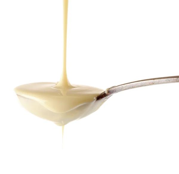 Condensed milk pouring from a spoon, isolated on white — Stock Photo, Image