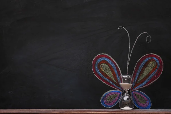 Concept of butterfly with hourglass and chalk on black background — Stock Photo, Image