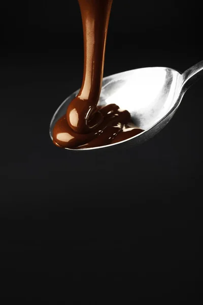 Coklat dituangkan pada sendok pada latar belakang gelap — Stok Foto