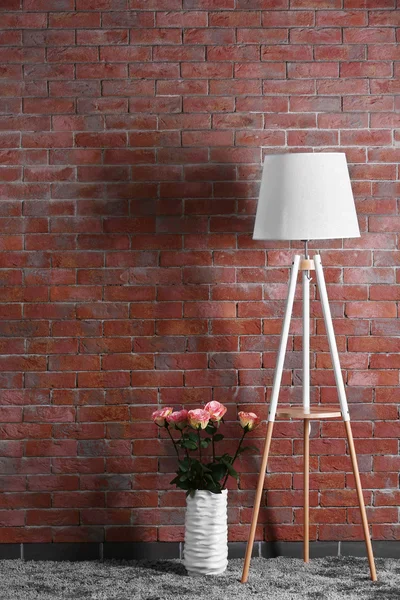 Weißer moderner Stuhl mit Lampe und Rosenstrauß auf Backstein-Hintergrund — Stockfoto