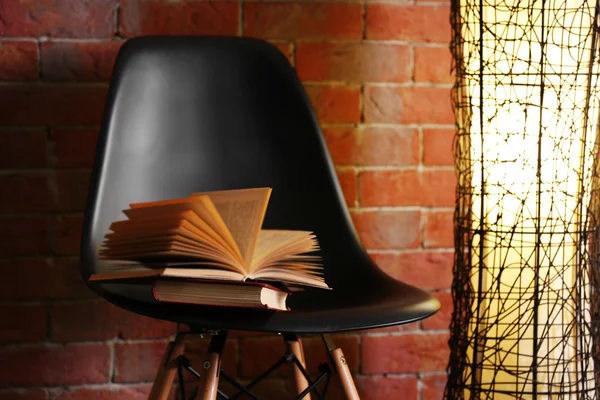 Black modern chair with lamp and books on brick wall background, close up — Stock Photo, Image