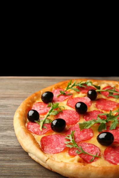 Ízletes pizza, szalámi és olajbogyó, fából készült tábla, fekete háttér ellenében — Stock Fotó