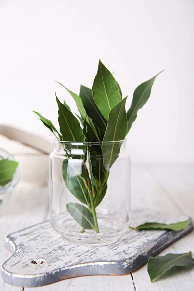 Foglie di alloro fresche in vaso di vetro, su tavolo di legno bianco — Foto Stock