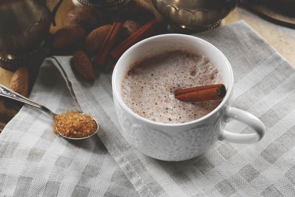 Cup of hot cacao on cotton serviette with cinnamon and almonds