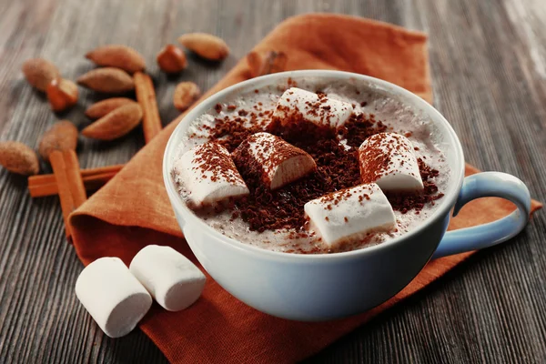 Tasse heißen Kakao mit Marshmallow, Zimt und Nüssen auf brauner Baumwollserviette, Nahaufnahme — Stockfoto