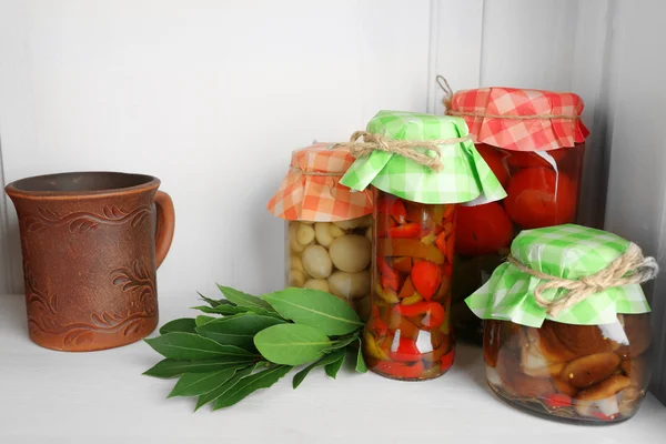 Jars with pickled vegetables and beans, spices, book of recipes and kitchen utensils on shelf — Stock Photo, Image