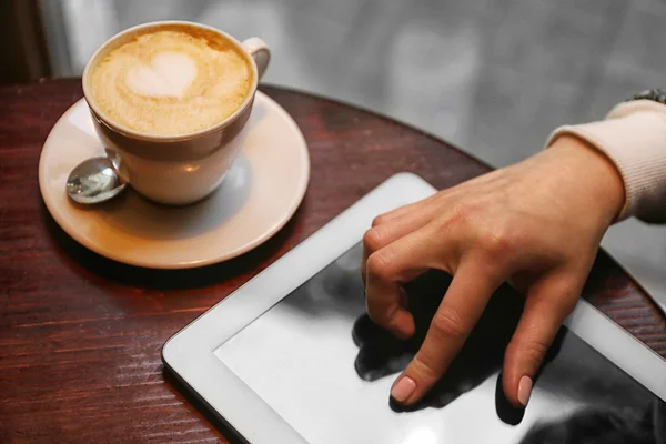 Girl hand with digital tablet and cappuccino on a wooden table — Stock Photo, Image