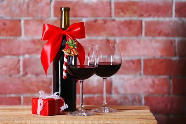Láhev červeného vína a brýle s vánoční dárky na zeď na pozadí — Stock fotografie