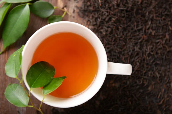Taza de té de cerámica con hojas de té dispersas sobre fondo de madera — Foto de Stock