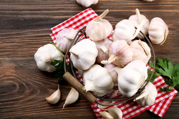 Fresh garlic in the basket decorated with parsley and red checkered cotton napkin on wooden background — Stock Photo, Image
