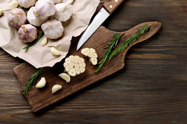 Samenstelling van knoflook en rozemarijn met mes op het bord van de keuken, close-up — Stockfoto